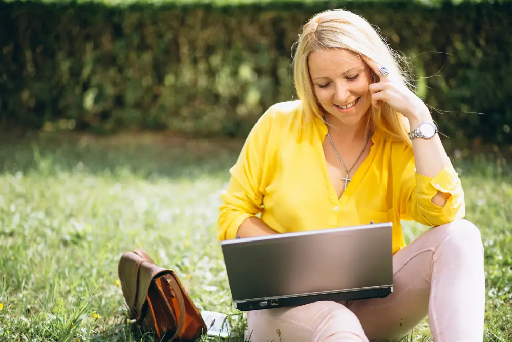 Une femme souriante, travaillant de manière flexible avec son ordinateur dans un parc, illustrant les avantages VDI.